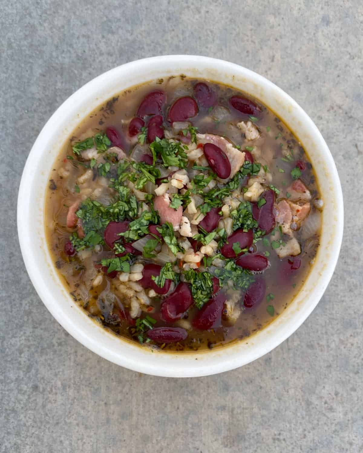 Jamaican Jerk seasoned red beans and rice soup garnished with chopped cilantro in white bowl.