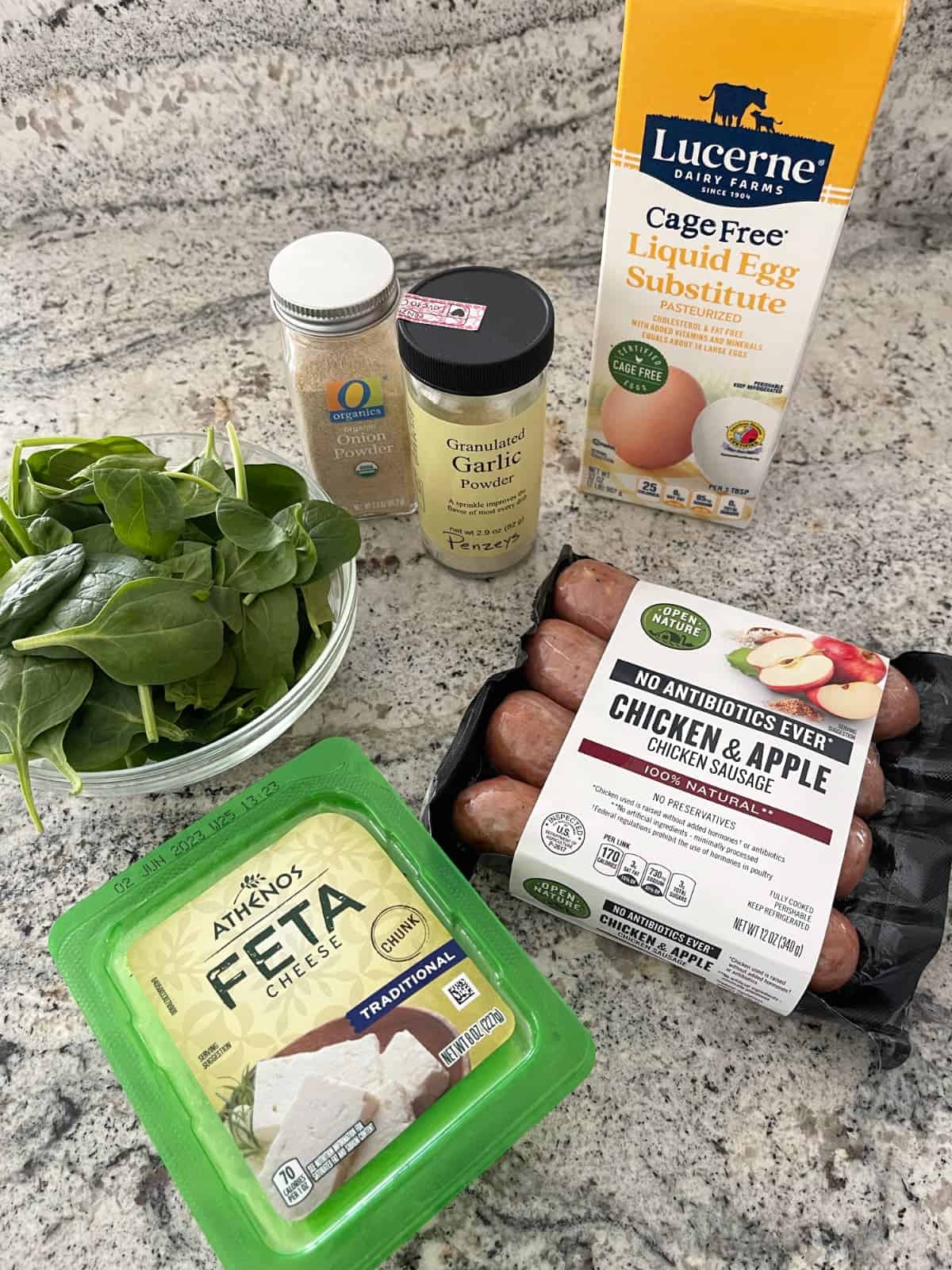 Ingredients including liquid egg substitute, chicken apple sausage, feta cheese, spinach, onion and garlic powder on granite.
