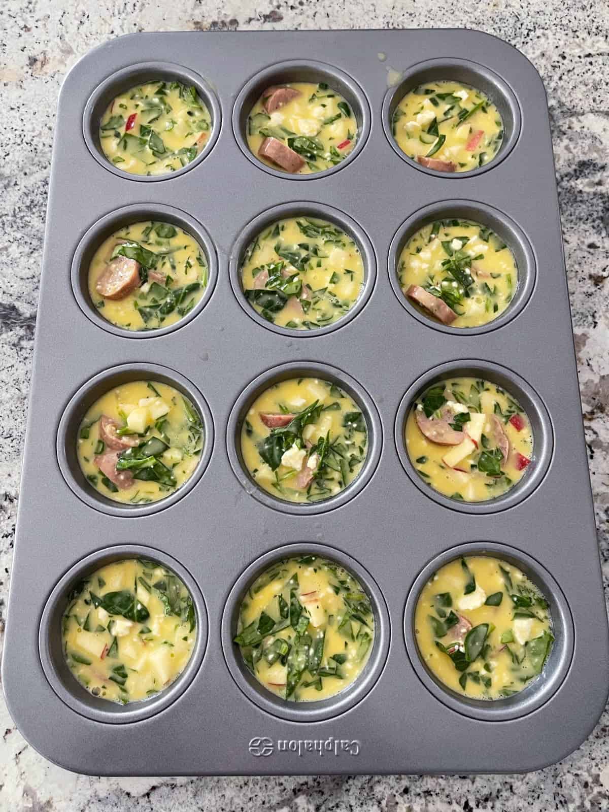 Unbaked apple chicken sausage egg bakes in muffin tin on granite counter.