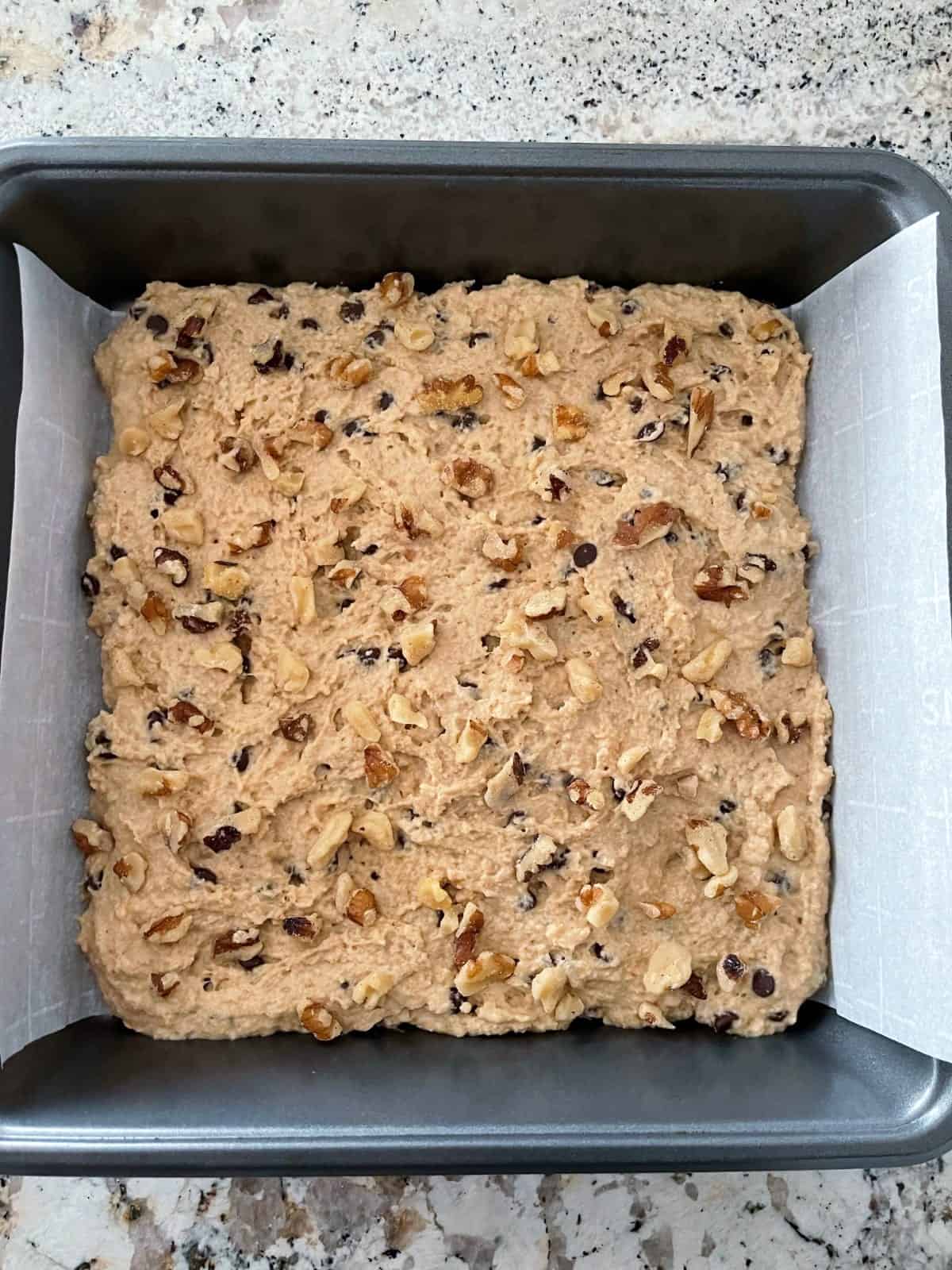 Unbaked chocolate chip Kodiak quick cake in parchment lined baking pan.