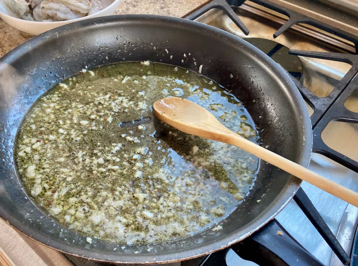 Butter, olive oil, garlic, crushed red pepper, salt and pepper simmering in a large nonstick skillet with wooden spoon.
