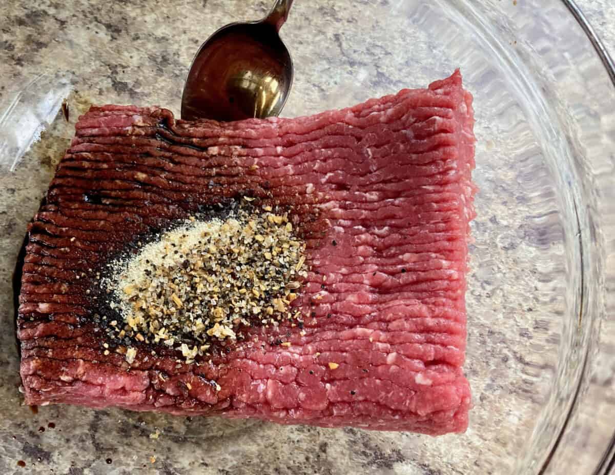 Ground beef and seasonings in a clear large mixing bowl.