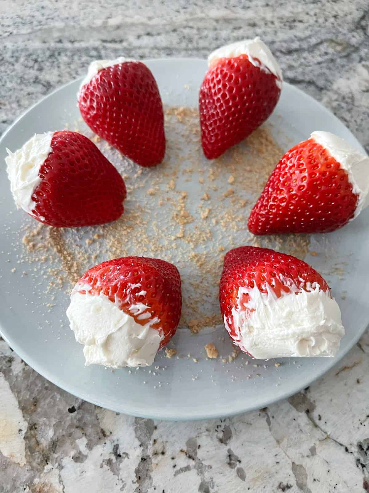 Cheesecake stuffed strawberries on round plate sprinkled with graham cracker crumbs.