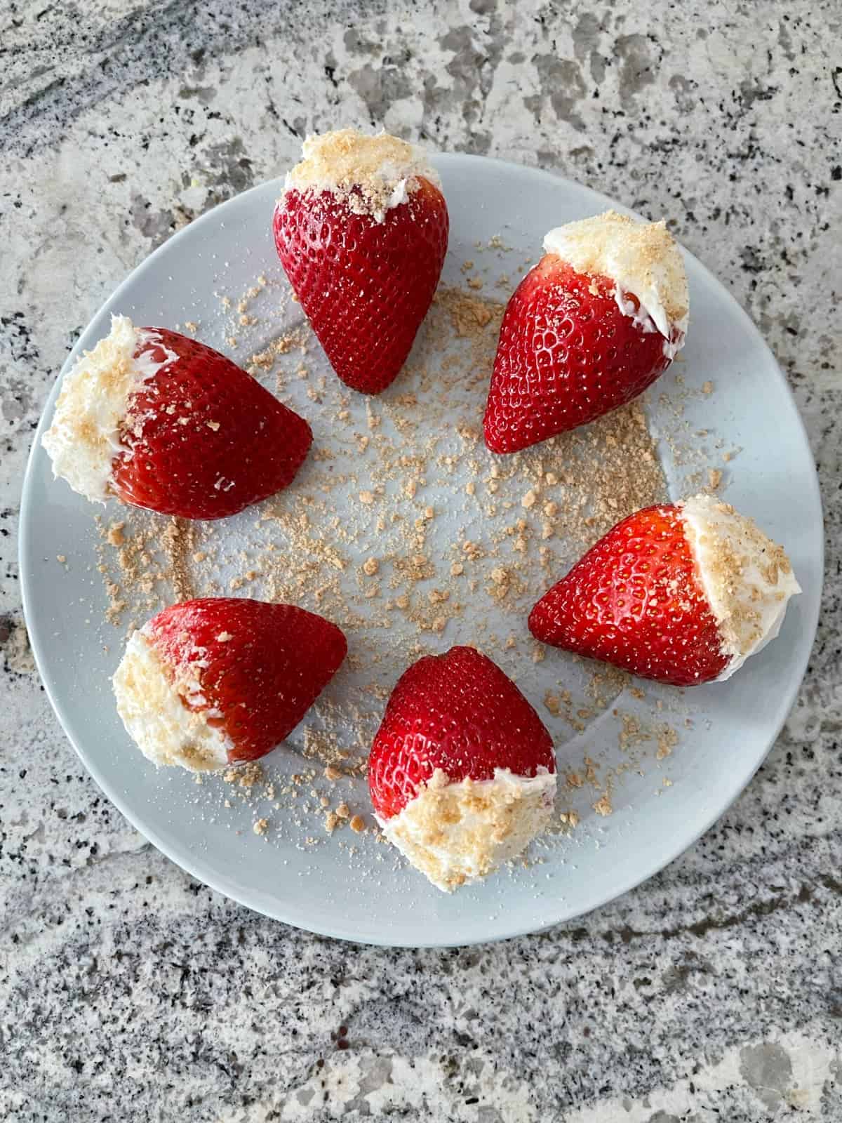 Cheesecake filled strawberries and topped with graham cracker crumbs on round serving plate.