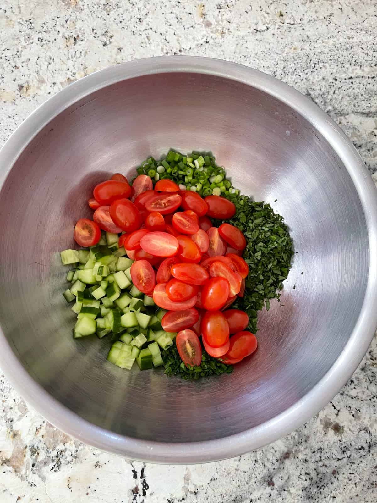 Halved cherry tomatoes, chopped cucumber, mint, parsley and green onions in mixing bowl.