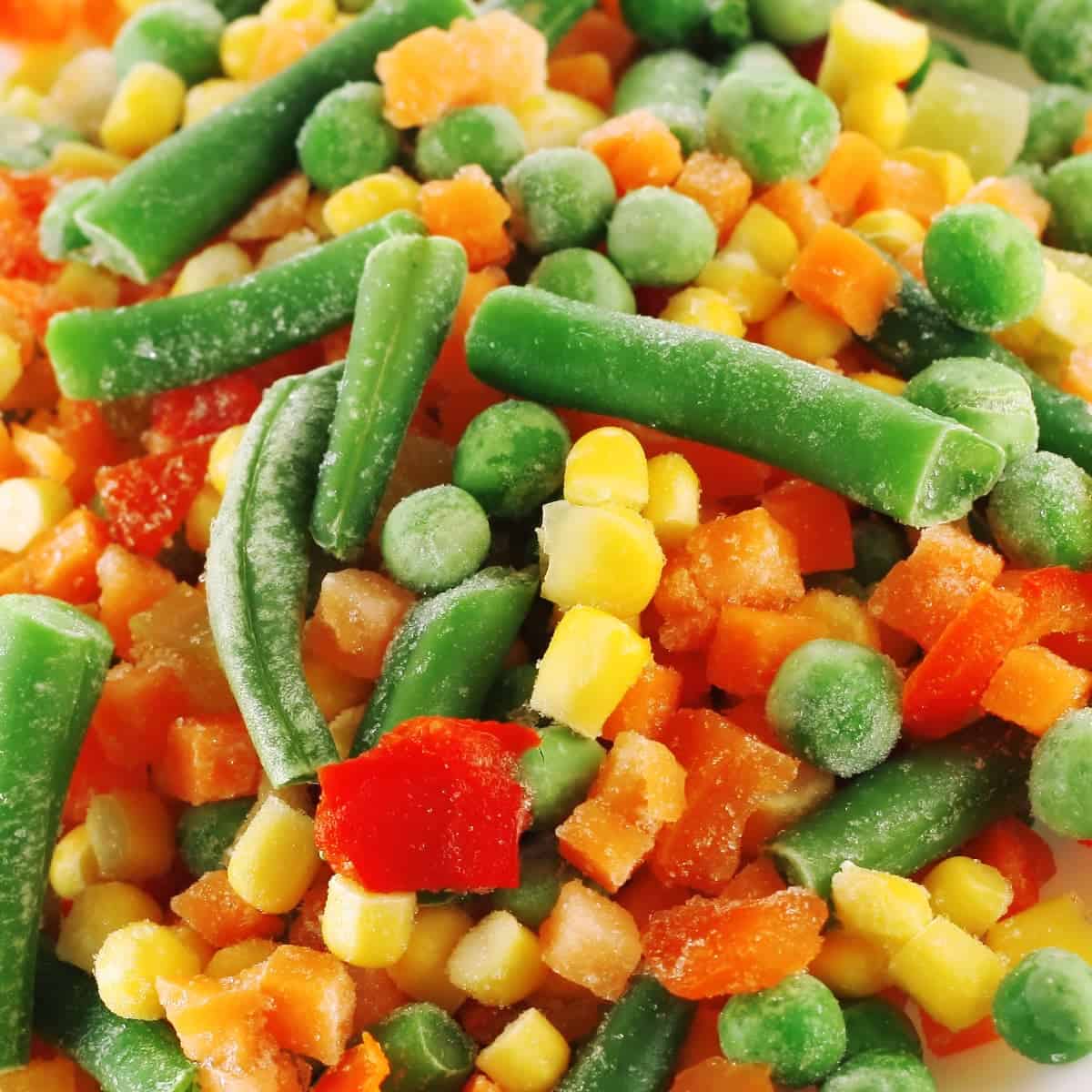 Close up of frozen mixed vegetables, including green beans, carrots, corn and peas.