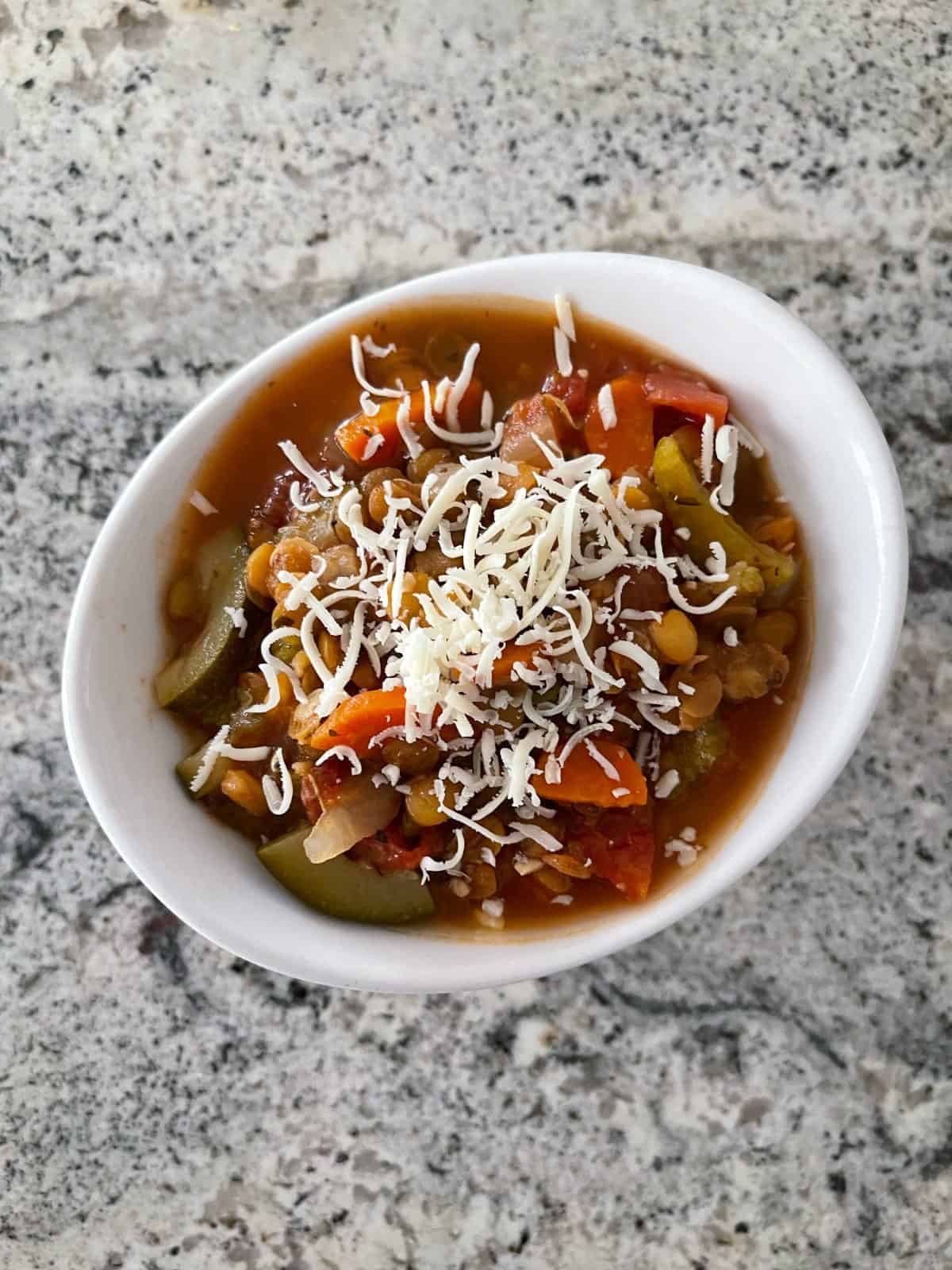 Vegetarian Lentil Minestrone topped with grated Parmesan cheese in white bowl.
