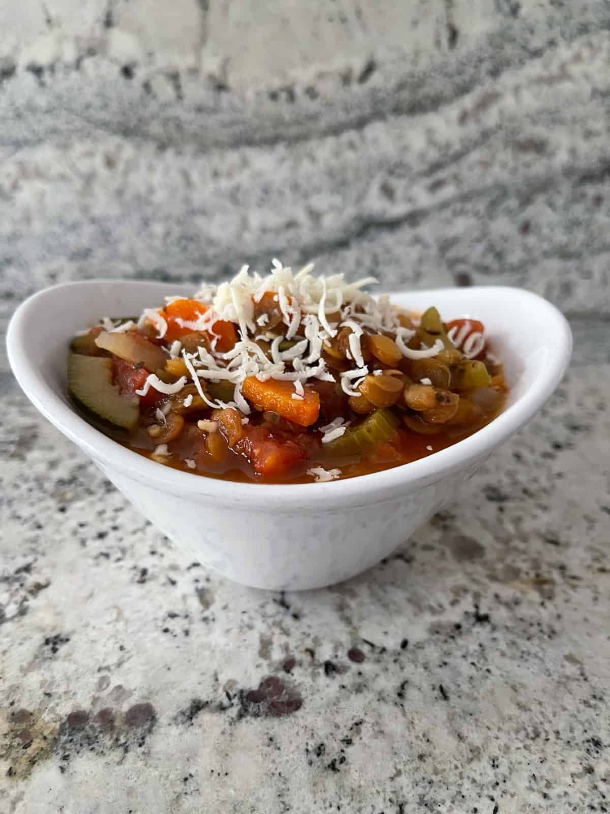 Instant Pot Lentil Minestrone topped with grated Parmesan cheese in white bowl on granite.