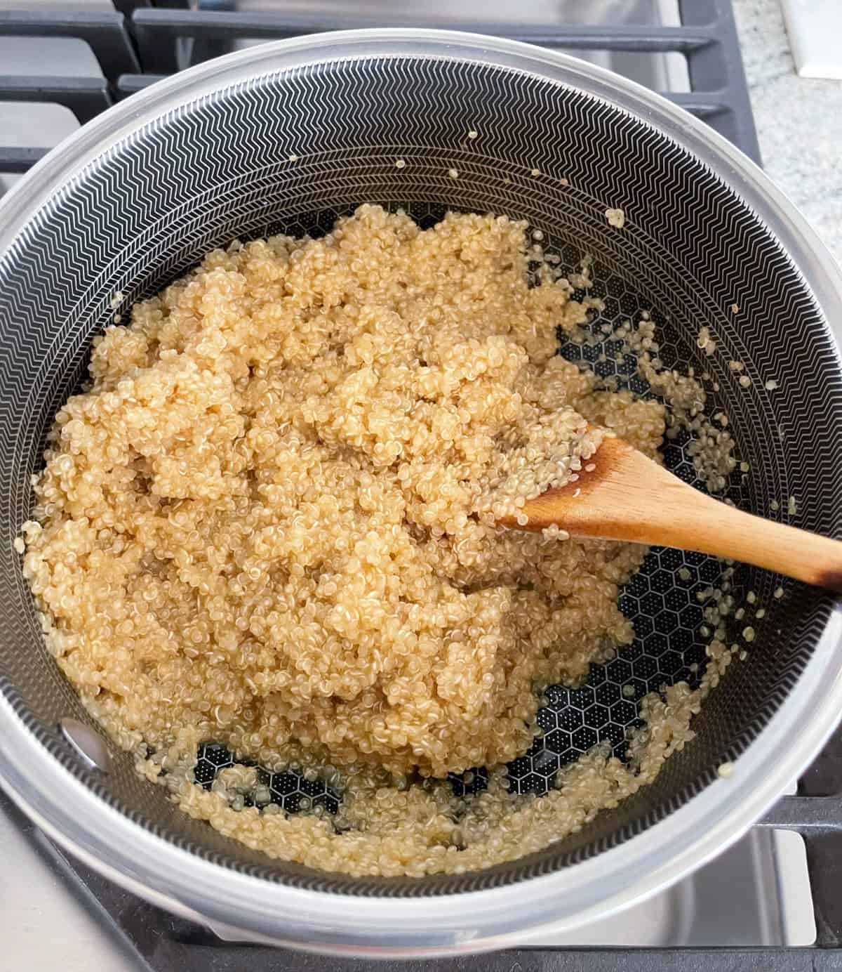 Stirring cooked quinoa in saucepan with wooden spoon.