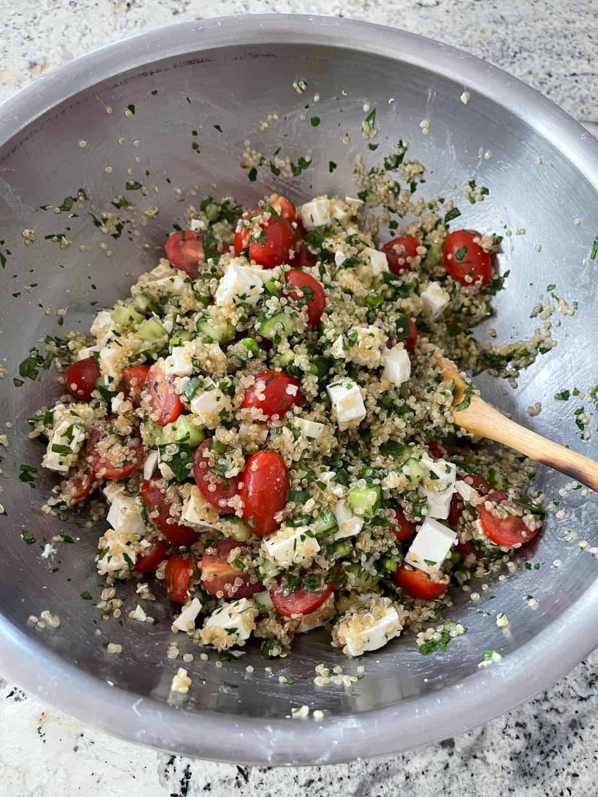 Mixing quinoa tabbouleh with fat-free feta cheese in bowl with wooden spoon.