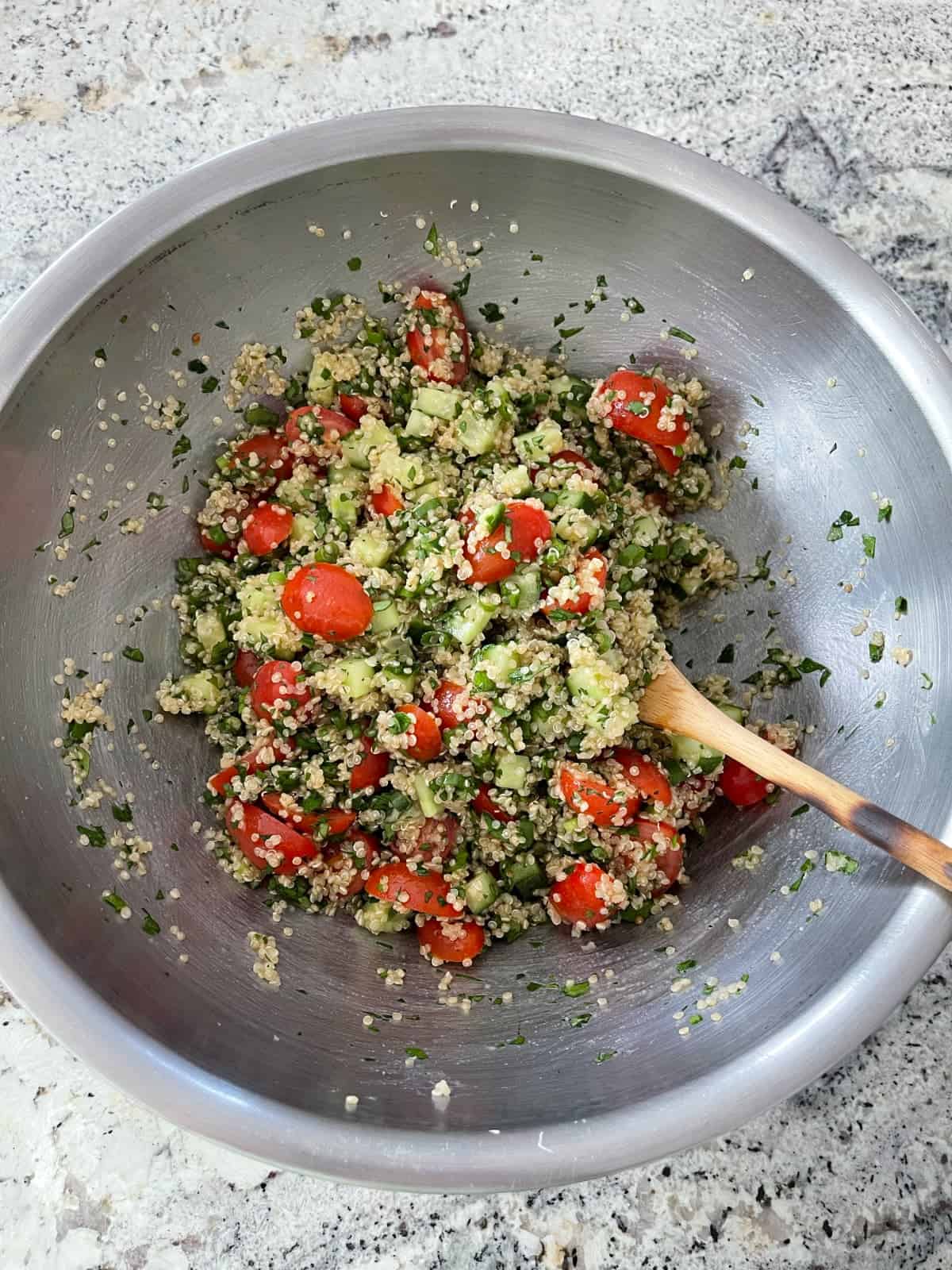 Stirring quinoa tabbouleh in mixing bowl with wooden spoon.