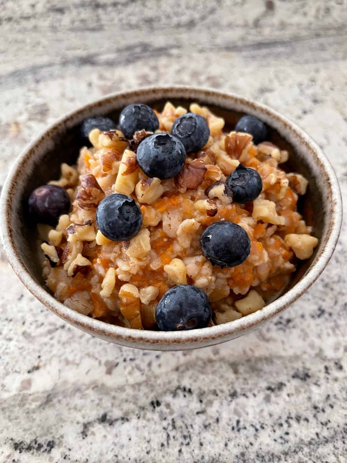 Carrot cake oatmeal topped with chopped walnuts and fresh blueberries in brown ceramic bowl.