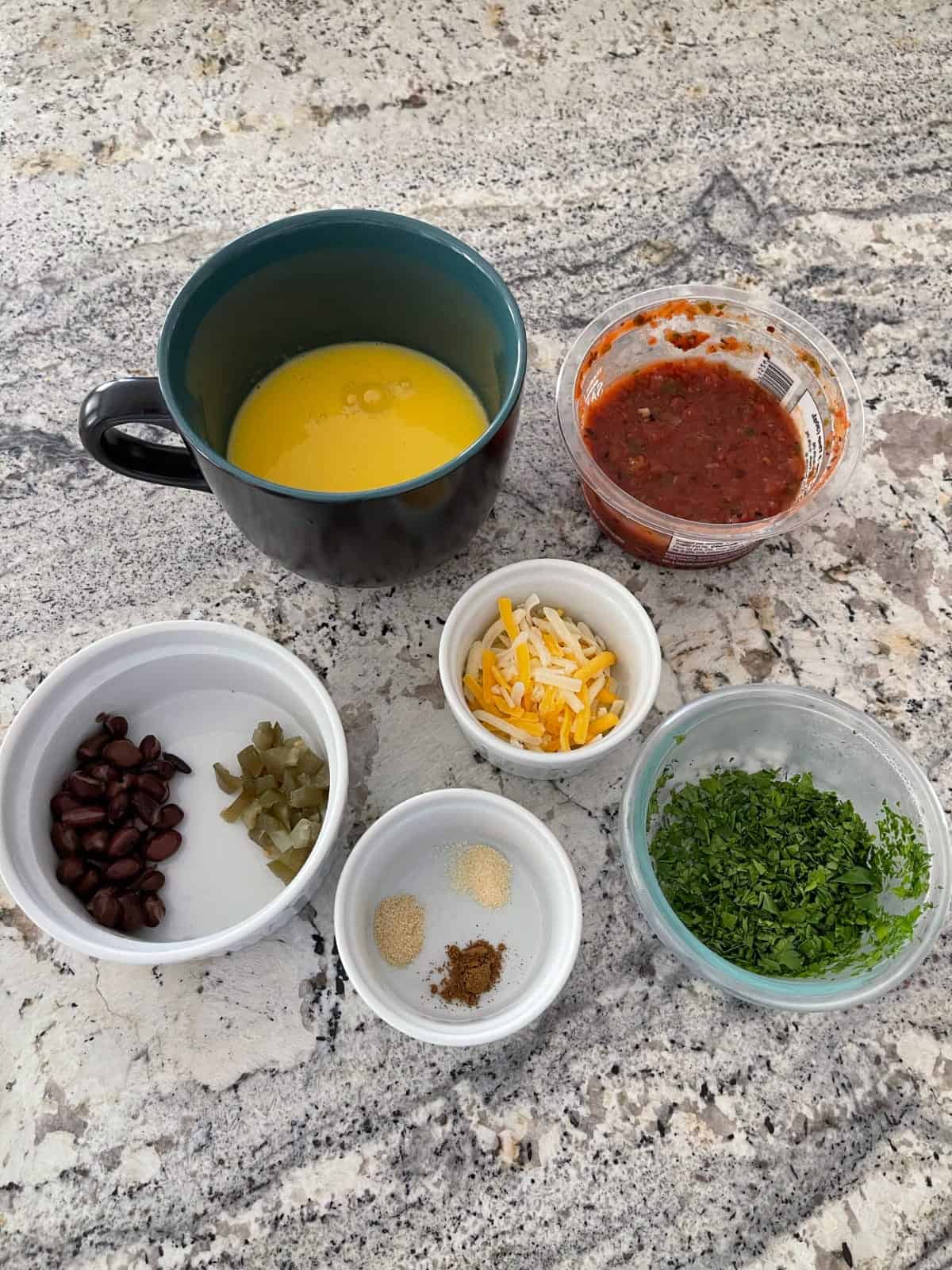 Ingredients for making Tex Mex Egg Mug including liquid egg substitute, salsa, shredded cheese, chopped cilantro, black beans, chopped jalapeños and spices.