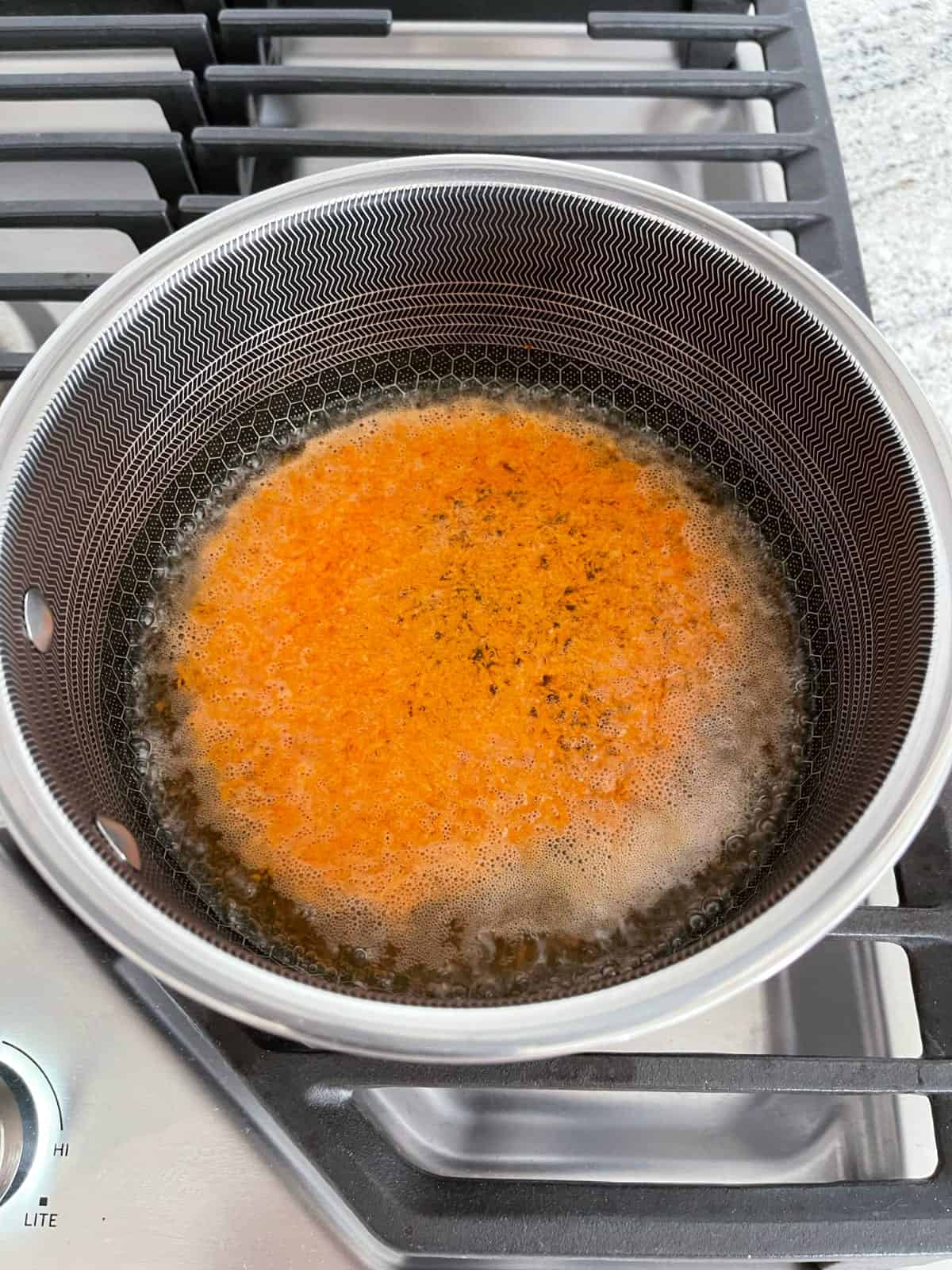 Simmering grated carrots in saucepan on stovetop.