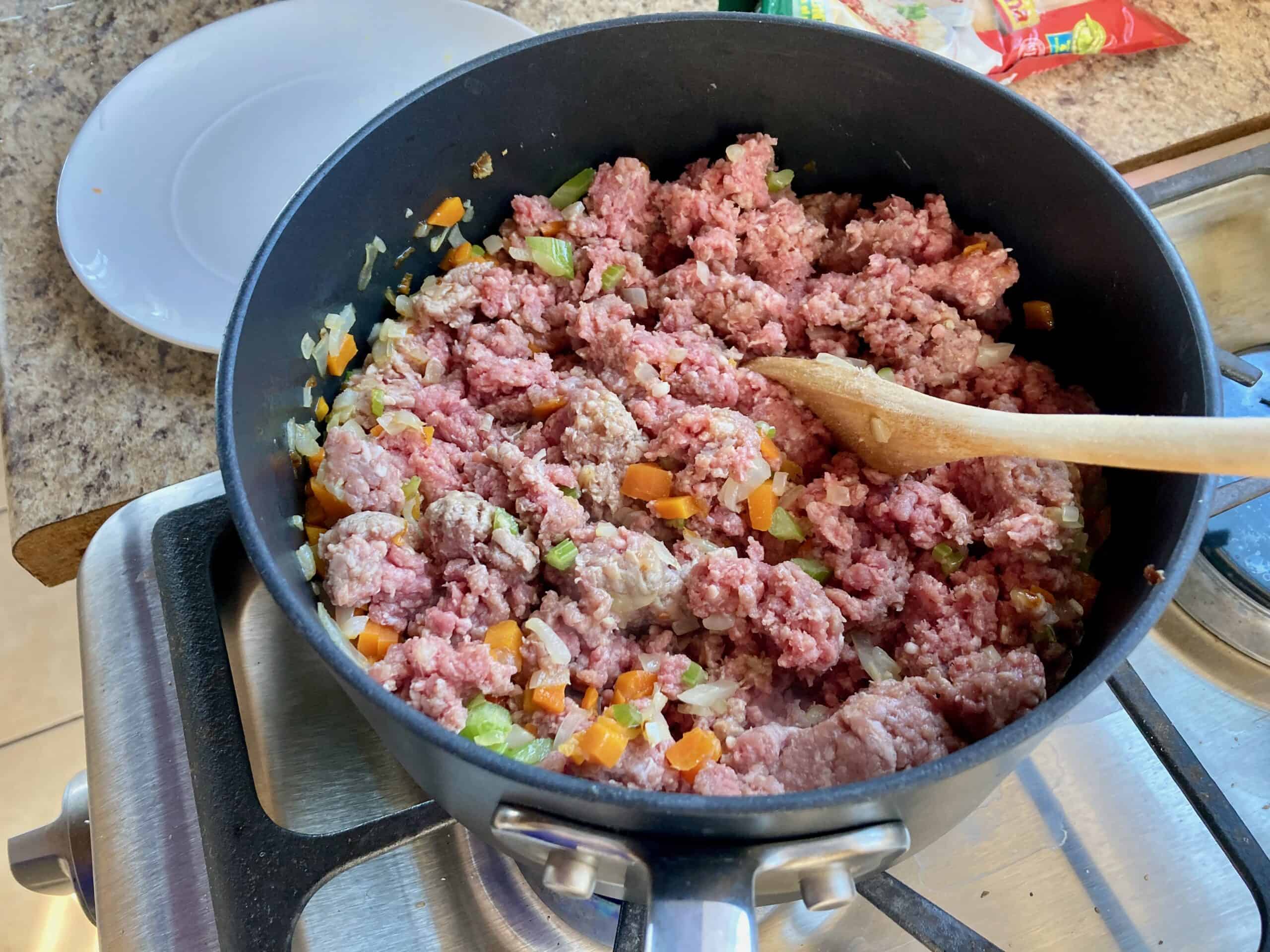 Ground turkey and vegetables in a pot with a wooden spoon on the stove.
