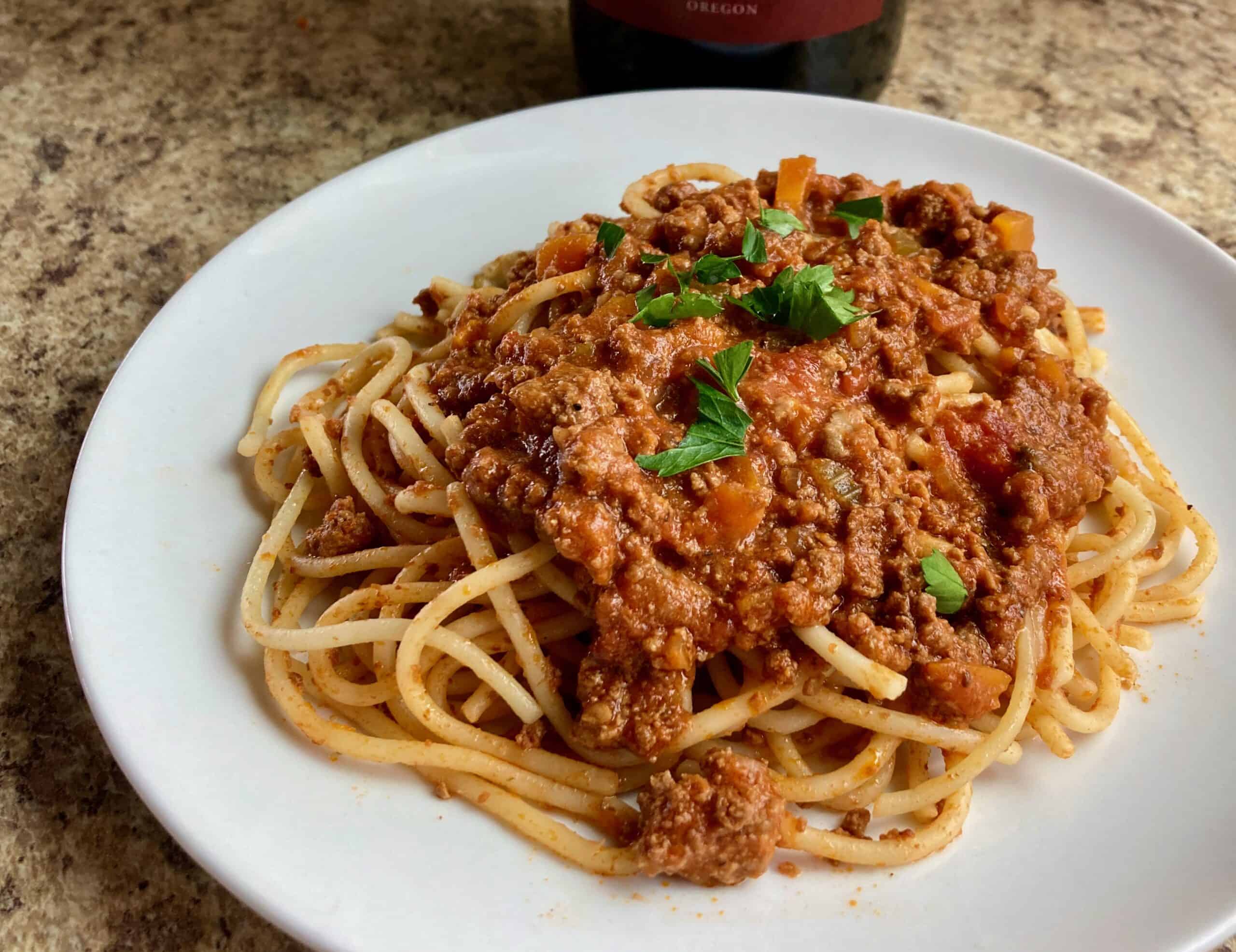 Slow Cooker Turkey Bolognese over spaghetti on white plate garnished with chopped parsley.