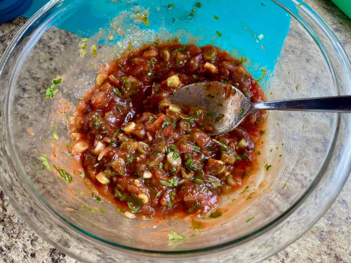 Stirring together shrimp salsa ingredients in a clear glass bowl.