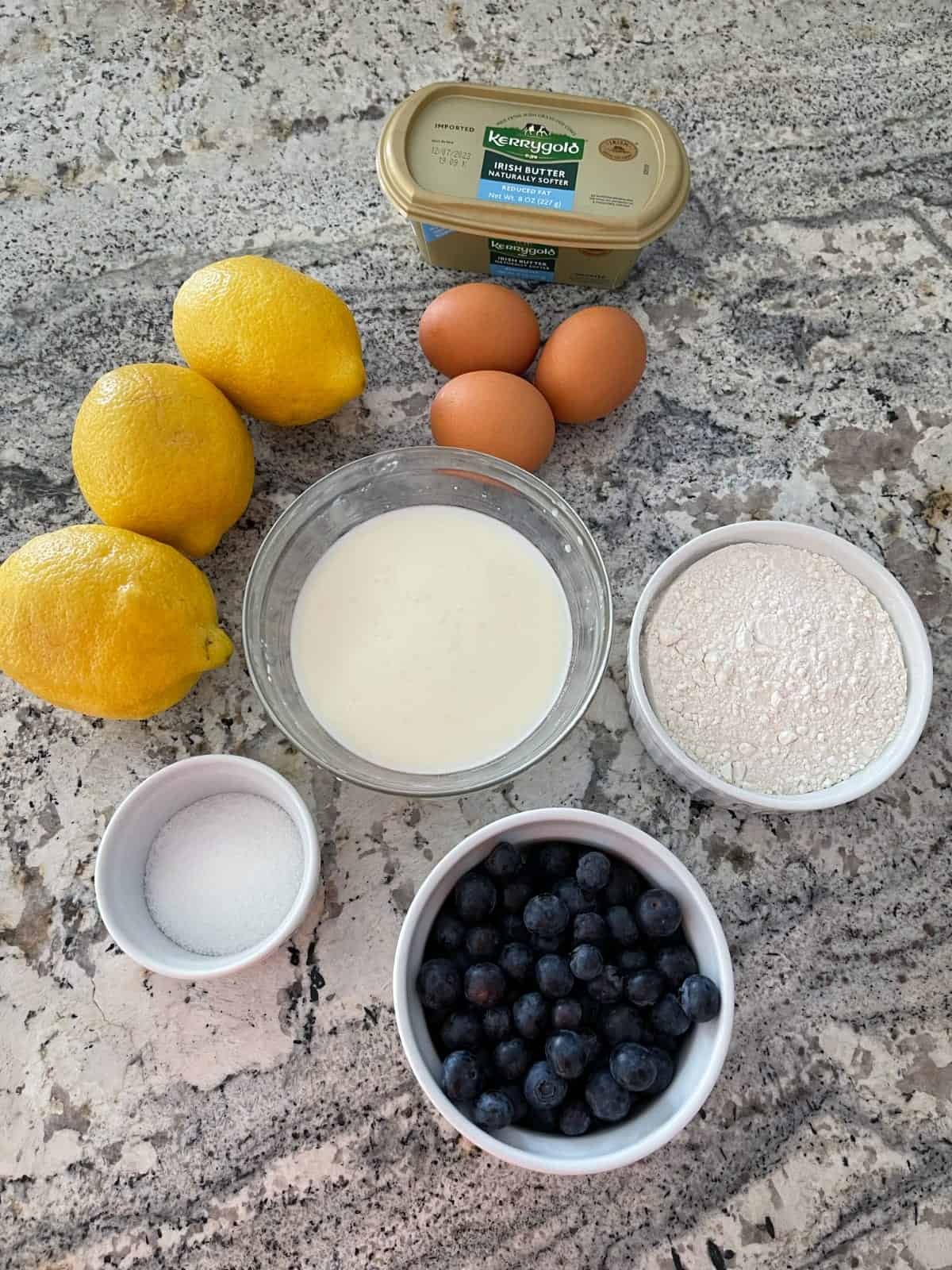 Ingredients including light butter, lemons, eggs, buttermilk, flour, blueberries and Truvia sweetener on granite.