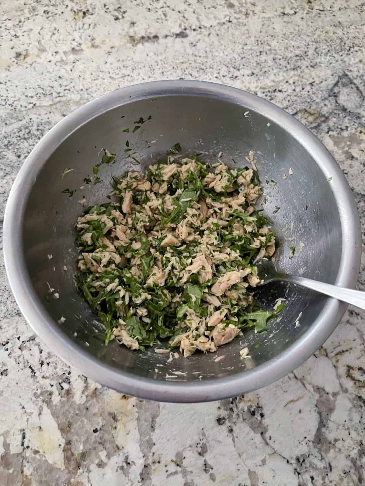 Mixing tuna with chopped arugula, minced basil, parsley and dill in mixing bowl with fork.