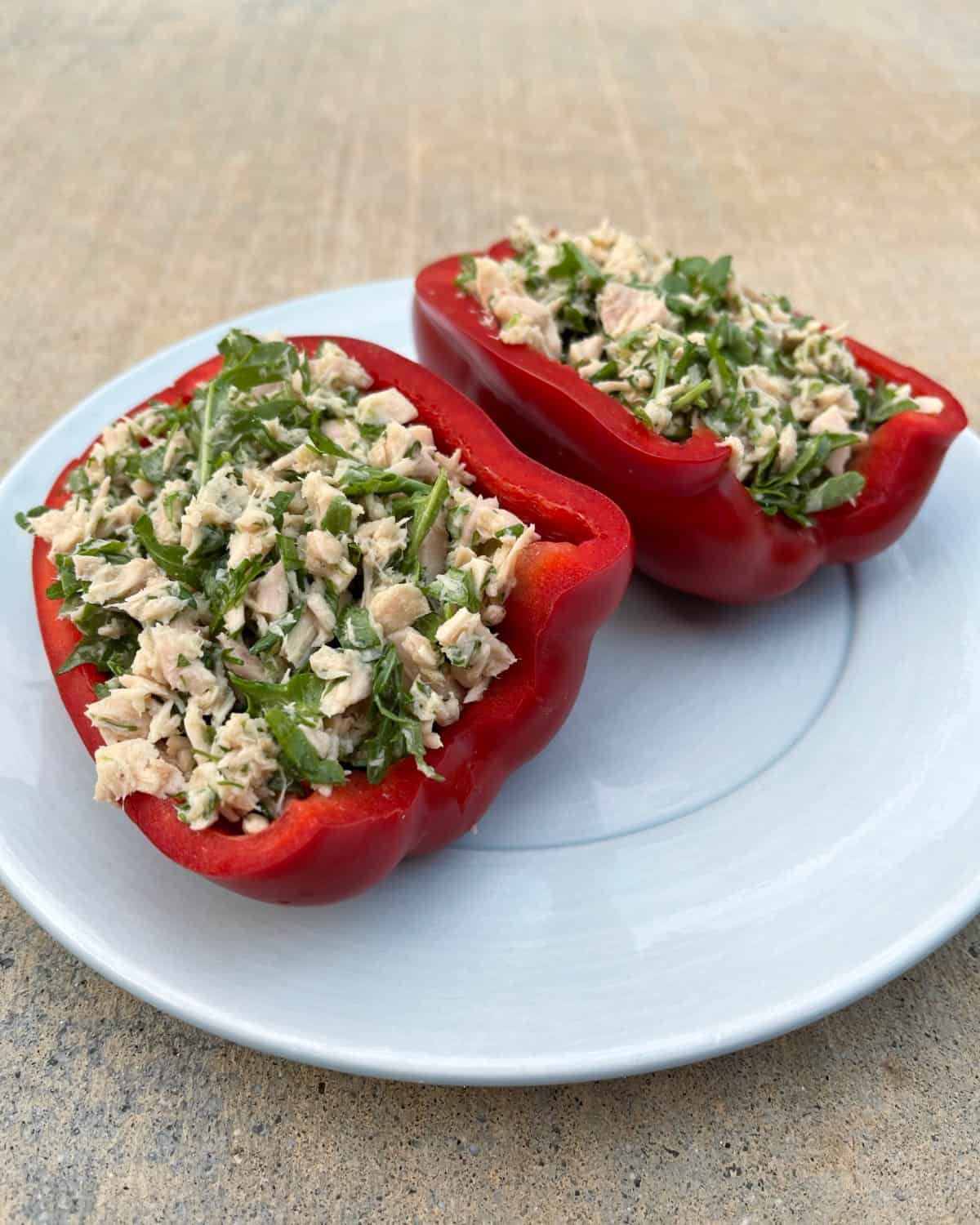 Red bell peppers stuffed with tuna and fresh chopped herbs on small blue plate.