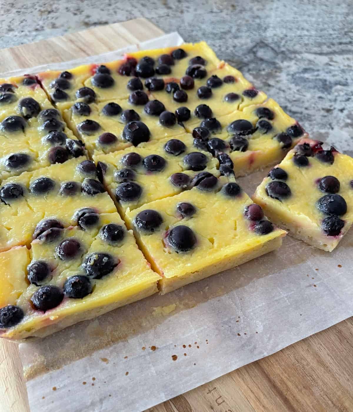 Lemon blueberry bars cut into 12 pieces on wood cutting board.