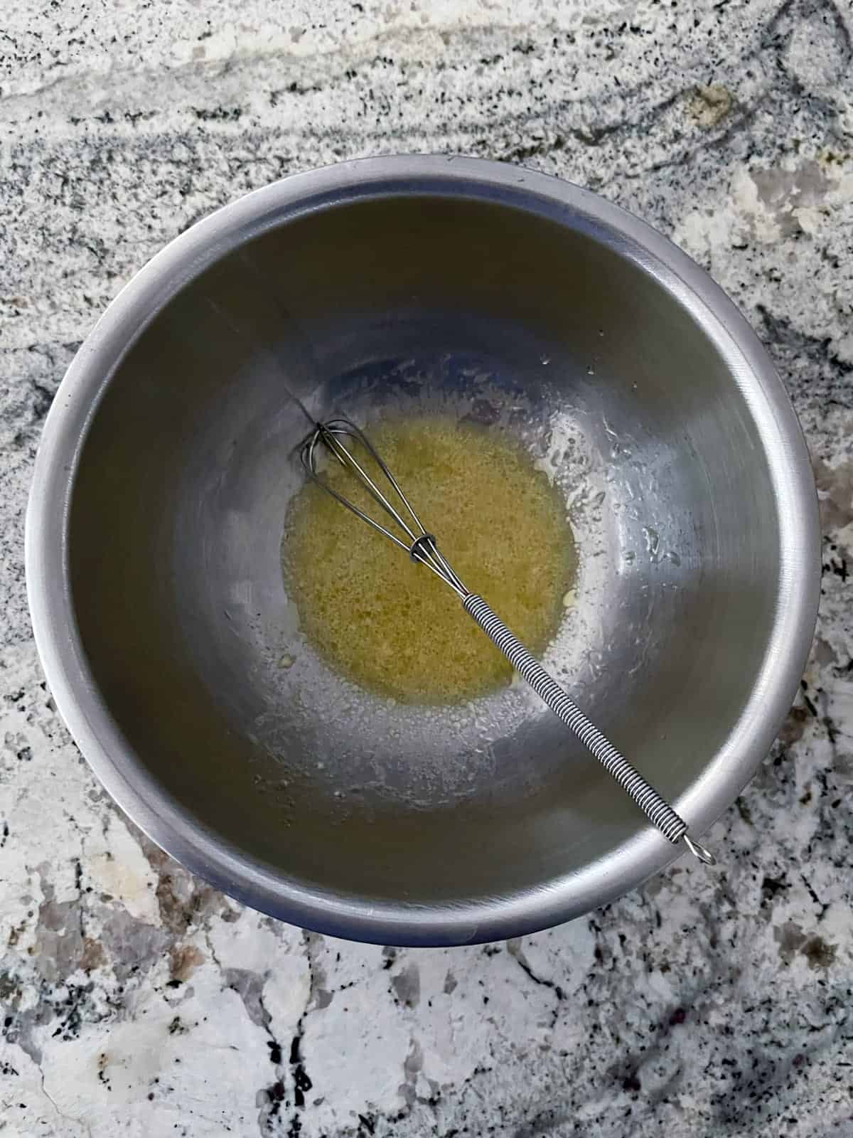 Whisking olive oil, lemon juice, dijon mustard, salt and pepper in mixing bowl.