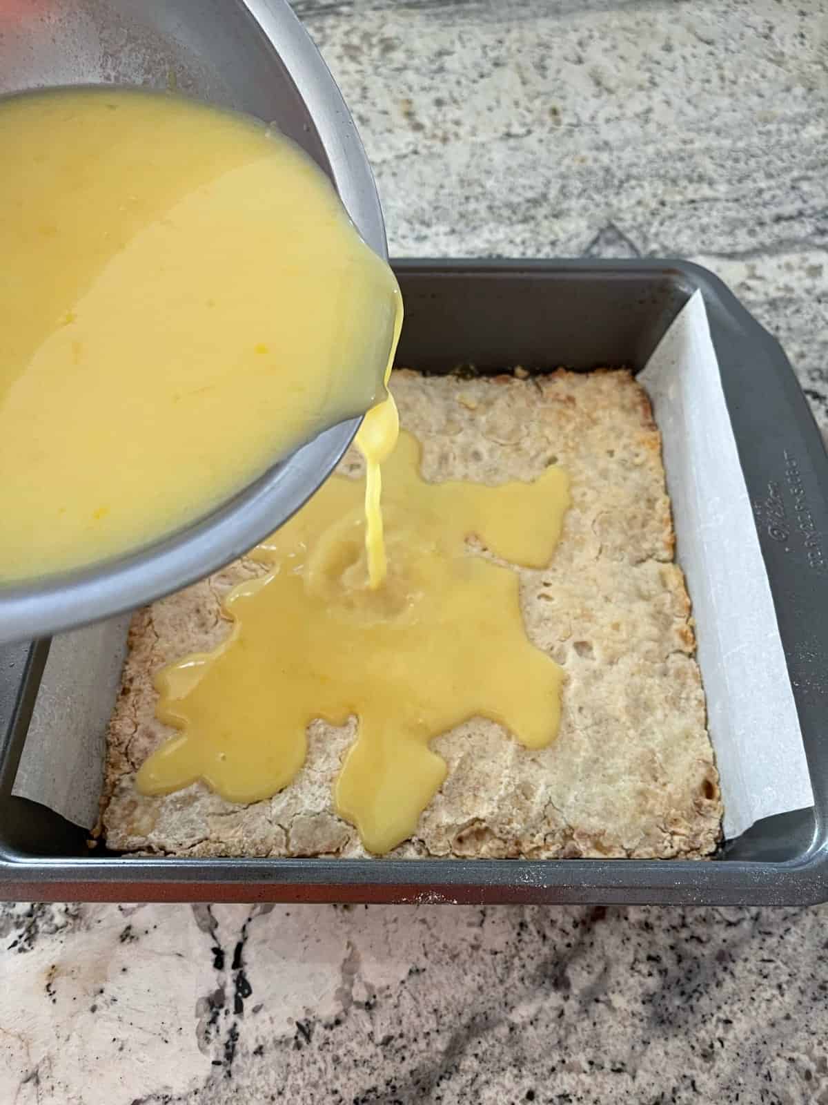 Pouring lemon bar topping over hot baked crust in baking pan.