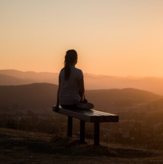 Woman sitting on a bench overlooking a canyon at sunrise