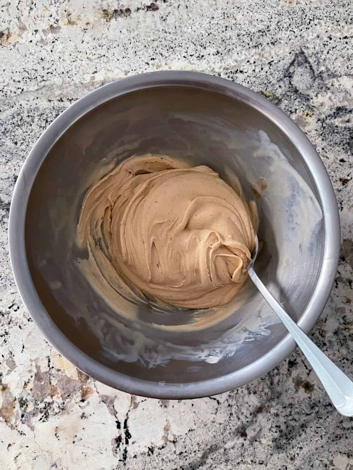 Stirring creamy peanut butter and vanilla ice cream in mixing bowl with spoon.