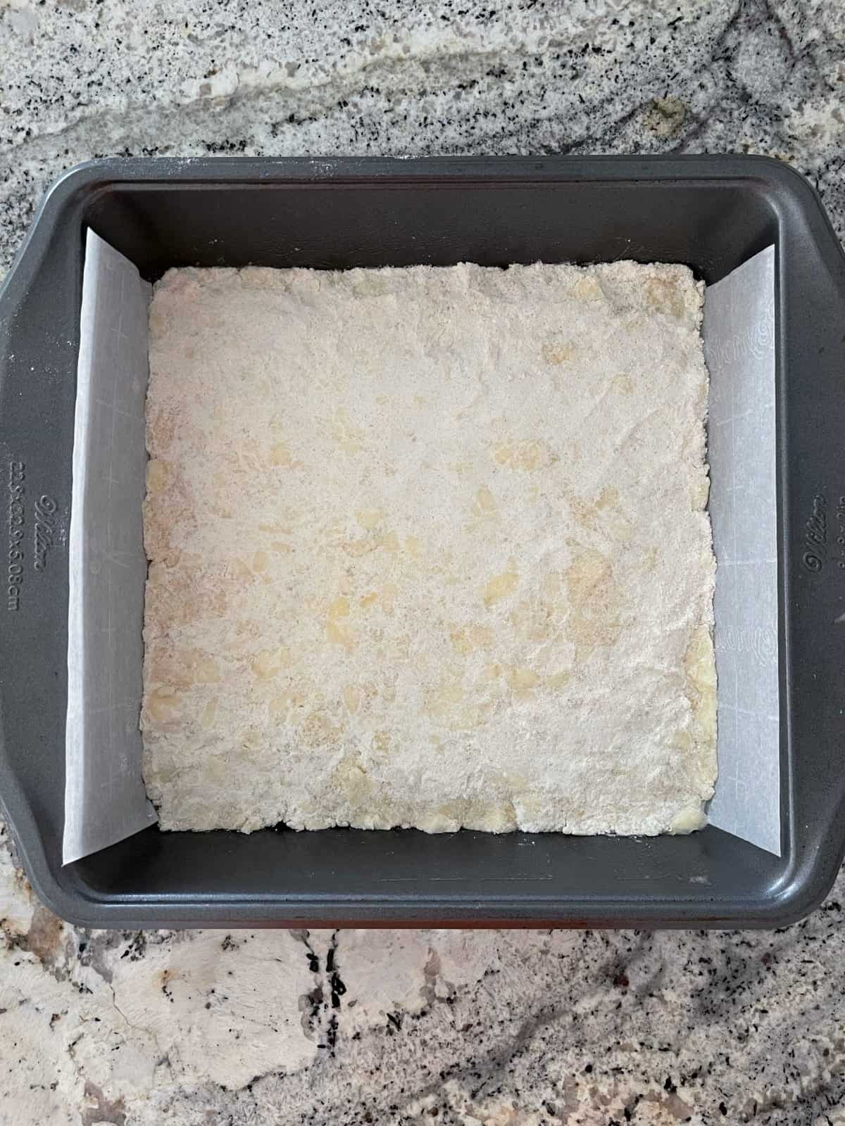Unbaked lemon zest in a square baking dish lined with parchment paper.
