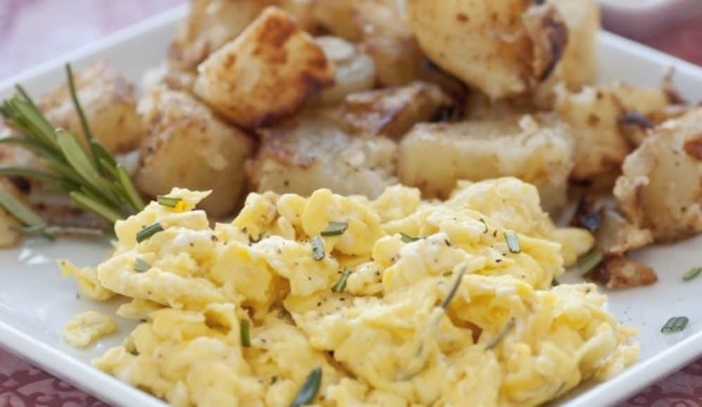 Scrambled Eggs and Breakfast Potatoes with fresh herbs up close on white plate.