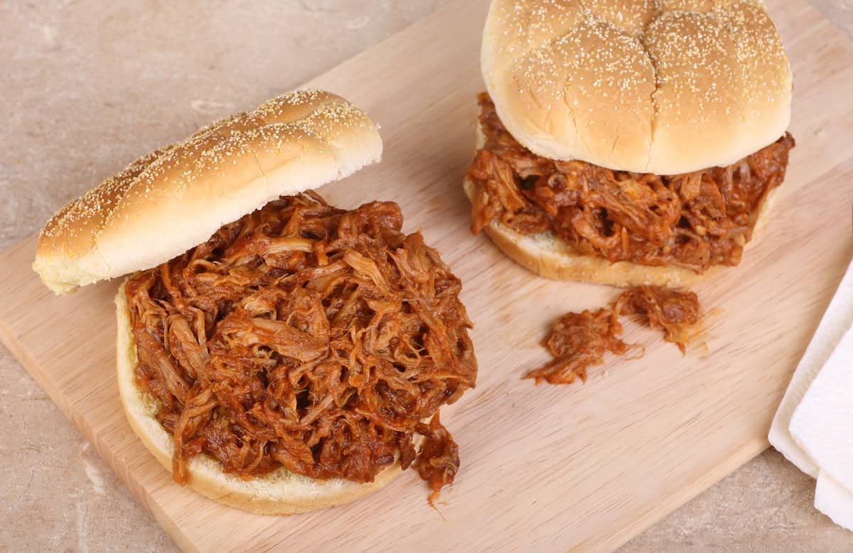 two pulled pork sandwiches on a light wood cutting board shot from above