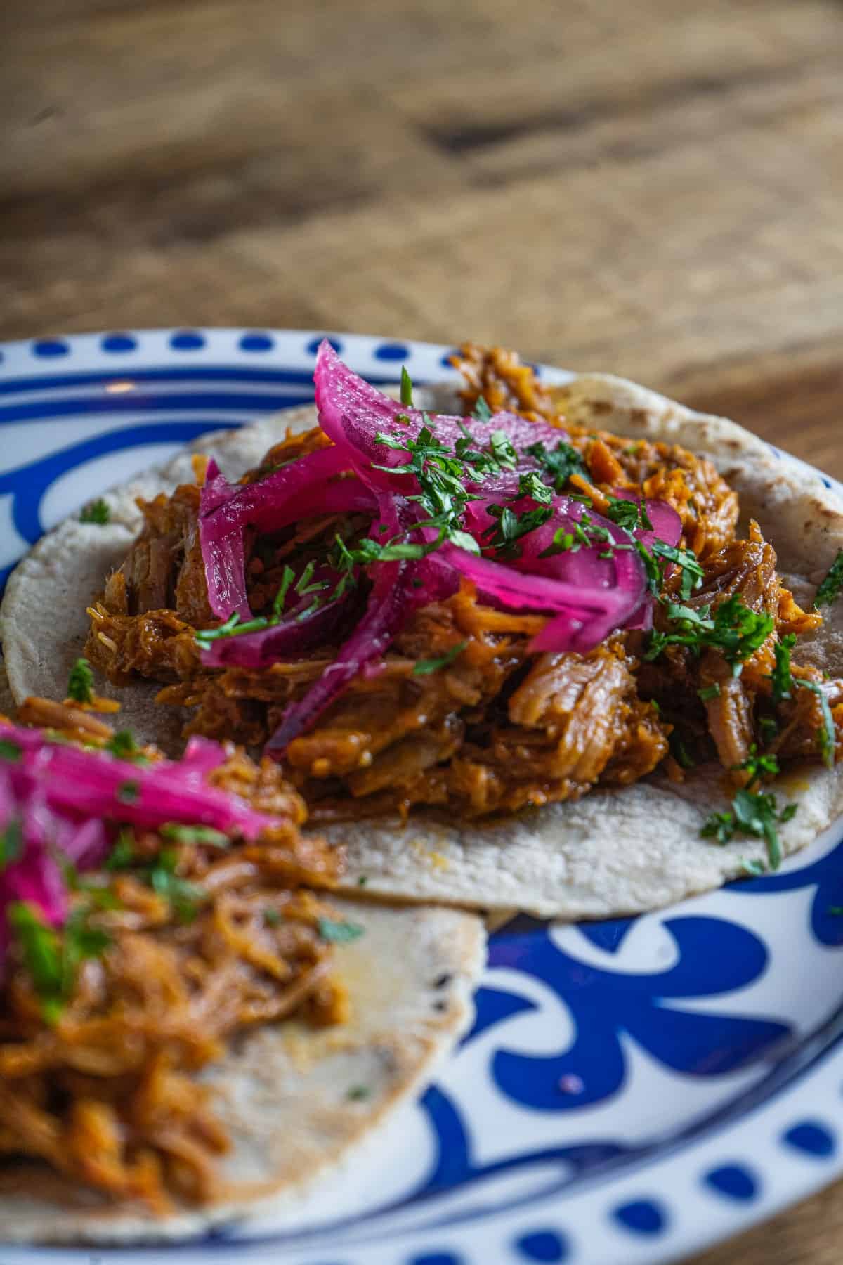 Cherry chipotle shredded pork tacos with pickled onions and cilantro on decorative blue and white plate.