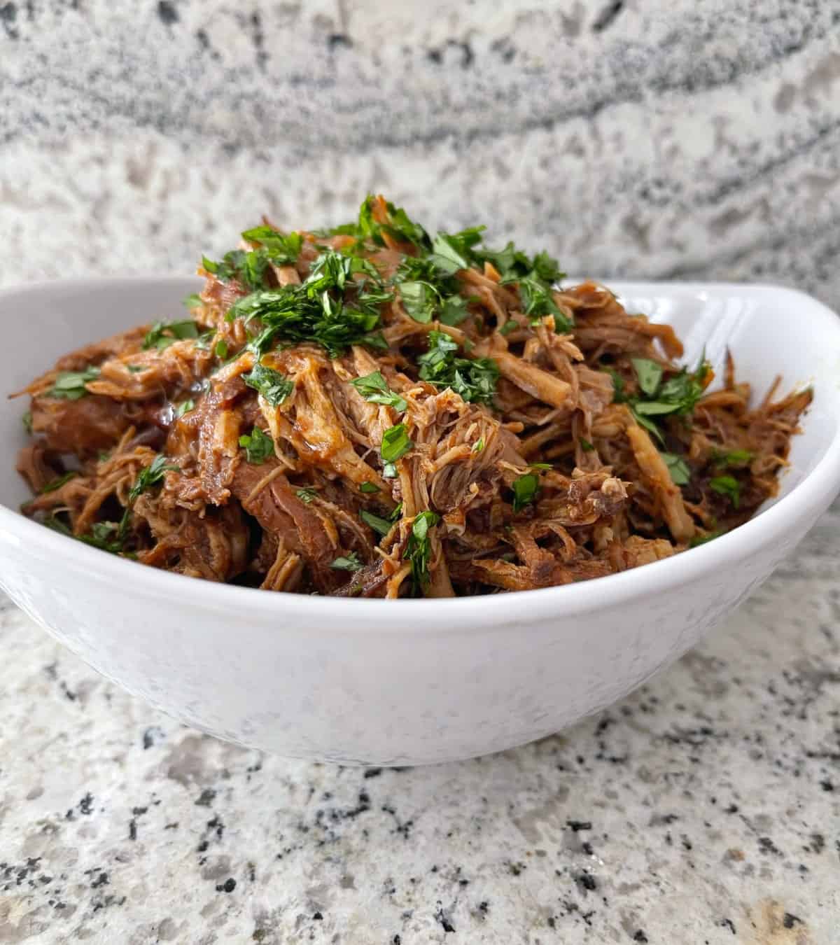 InstantPot Cherry Chipotle Shredded Pork topped with chopped cilantro in white serving bowl on granite.