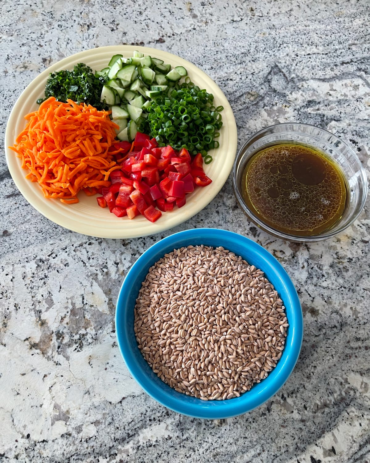Ingredients including farro, shredded carrots, chopped red bell pepper, cucumber, sliced green onions, chopped cilantro, olive oil and lime juice dressing.