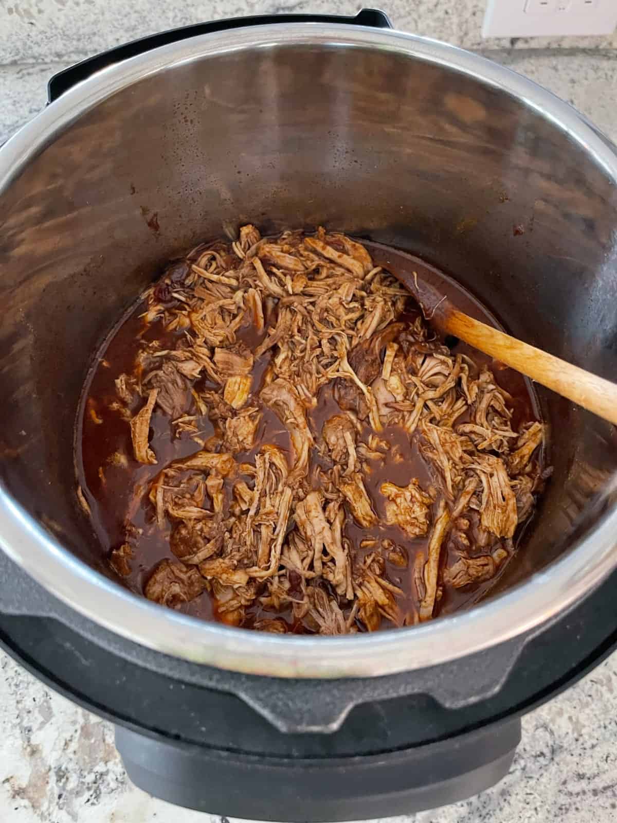 Cherry Chipotle Pulled Pork in InstantPot with wooden spoon.