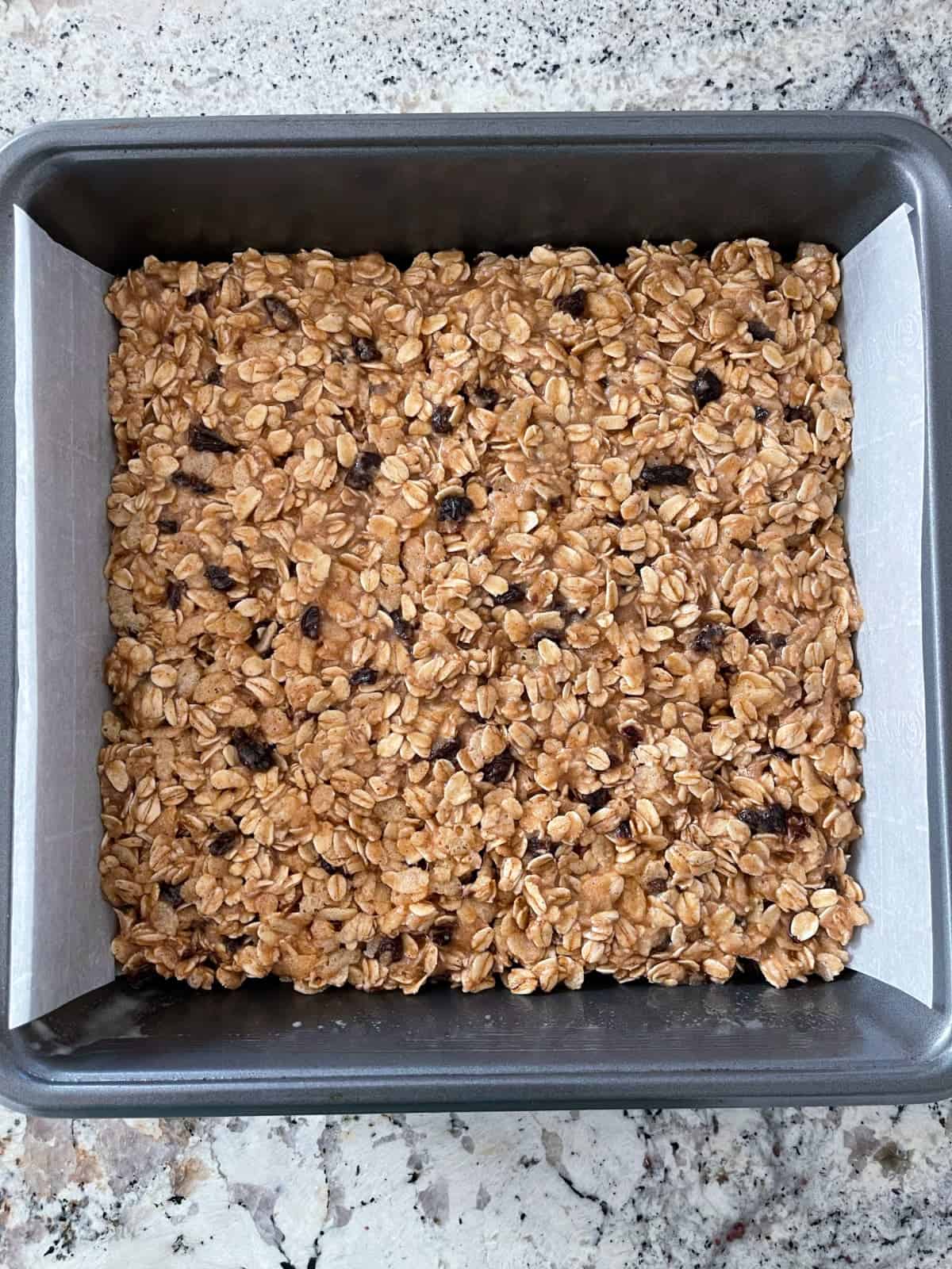 Unbaked oatmeal spice bars in parchment paper lined baking pan.