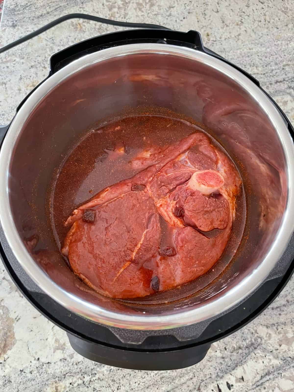 Uncooked pork shoulder smothered in cherry chipotle sauce in InstantPot pressure cooker.