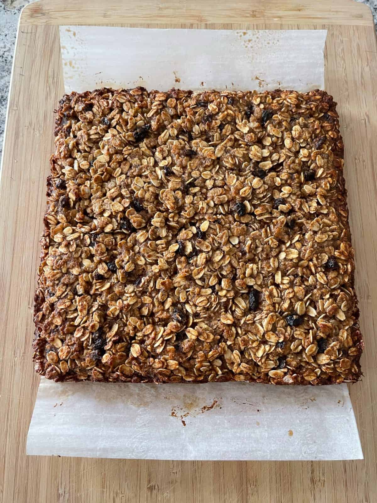 Fresh baked uncut oatmeal spice bars on parchment paper on wood cutting board.