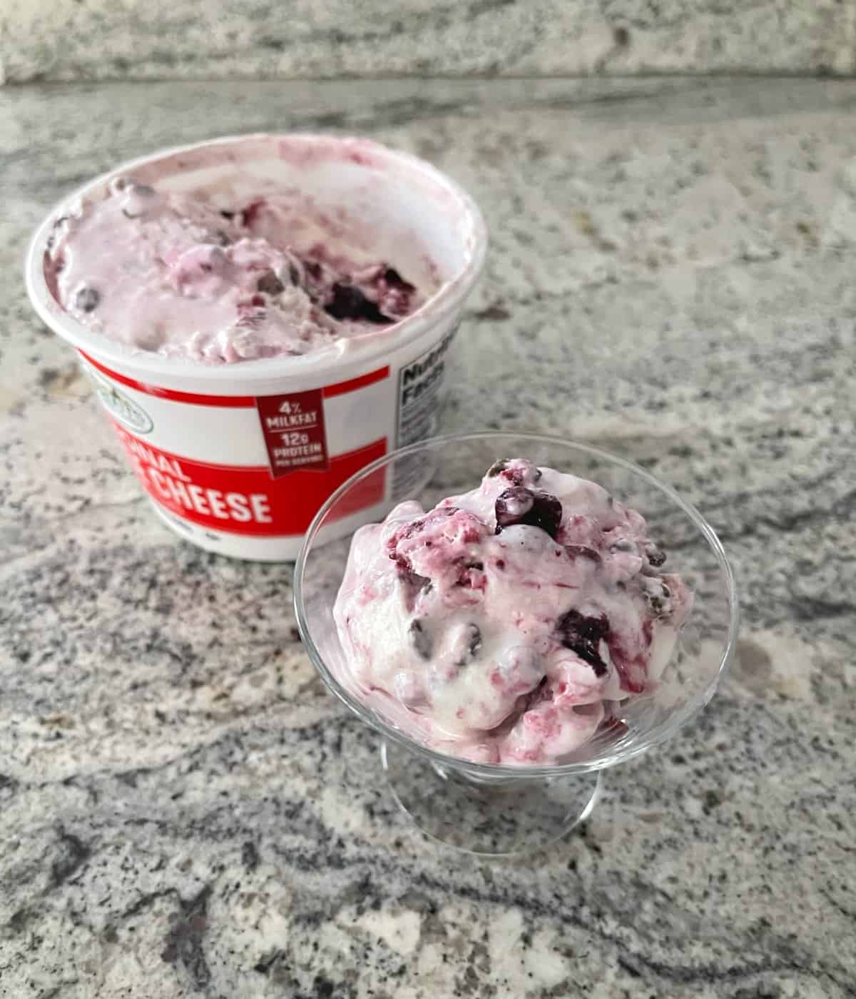 Container of homemade cherry chocolate chip cottage cheese ice cream with a scoop of ice cream in a small glass bowl in front.