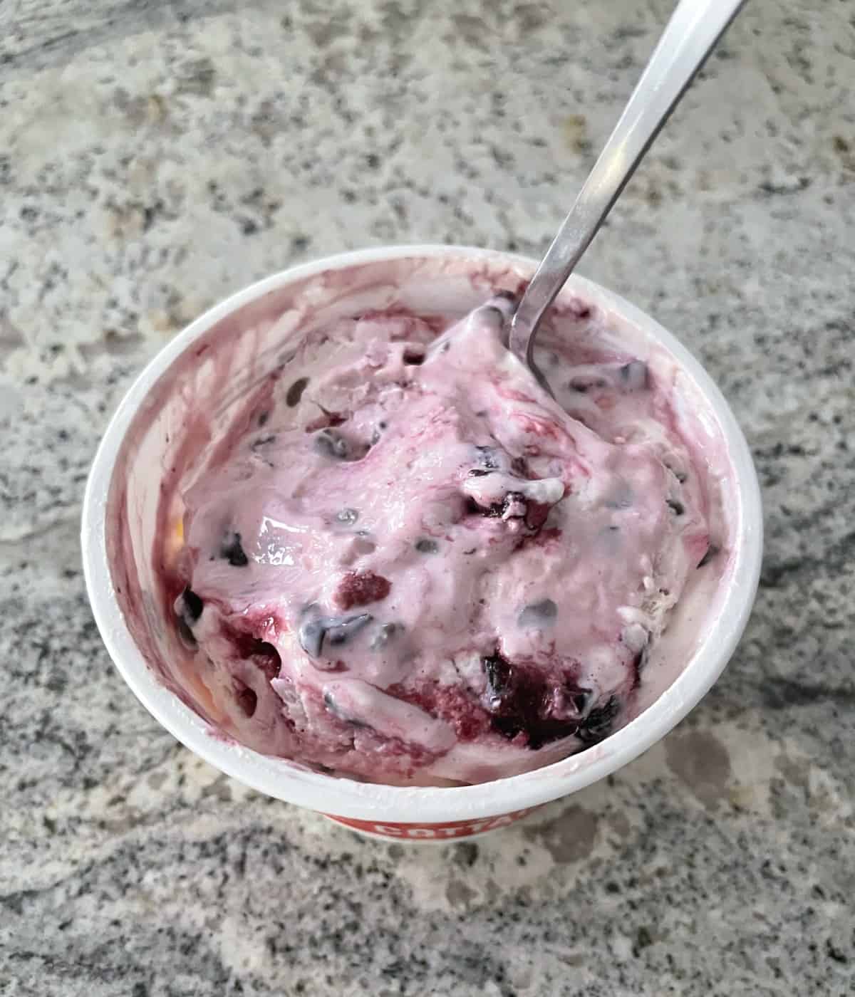 Container of homemade cottage cheese chocolate chip cherry ice cream with scoop.