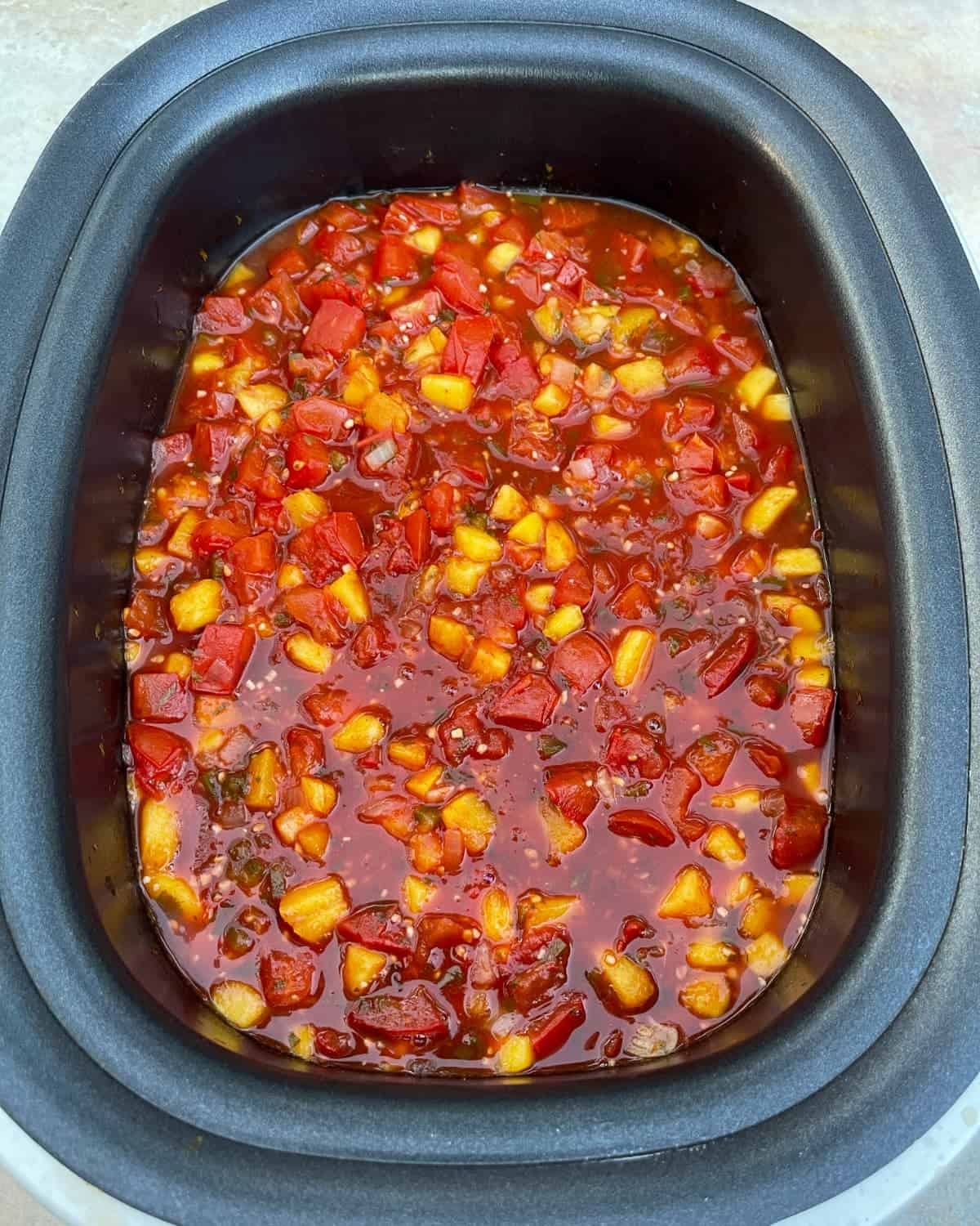Fresh cooked peach salsa in black slow cooker.