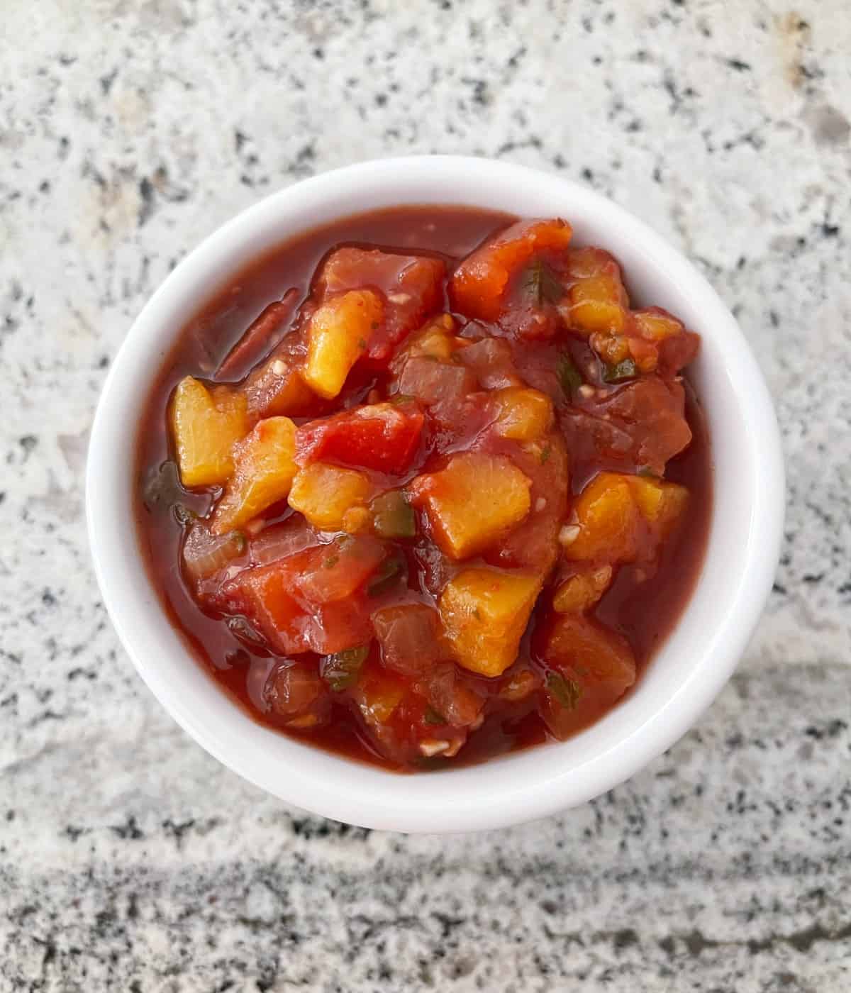 Slow cooked fresh peach salsa in small white bowl on granite.