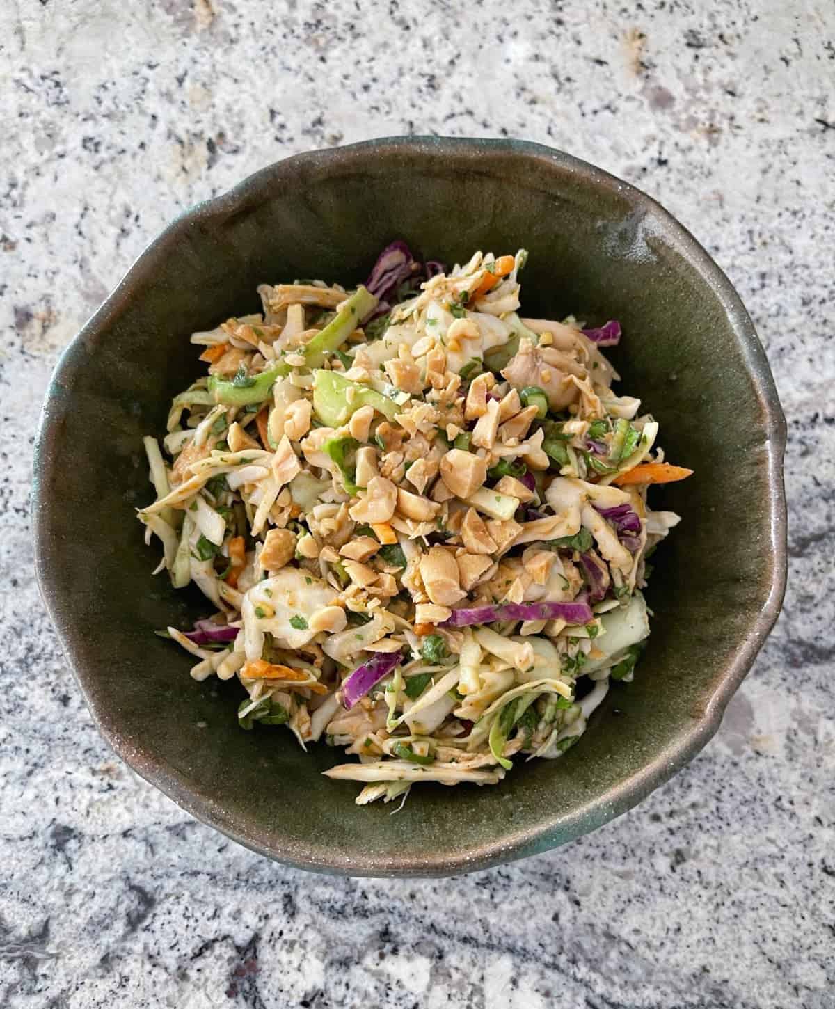 Fresh and crunchy Thai chicken coleslaw in a green ceramic bowl on a granite counter.