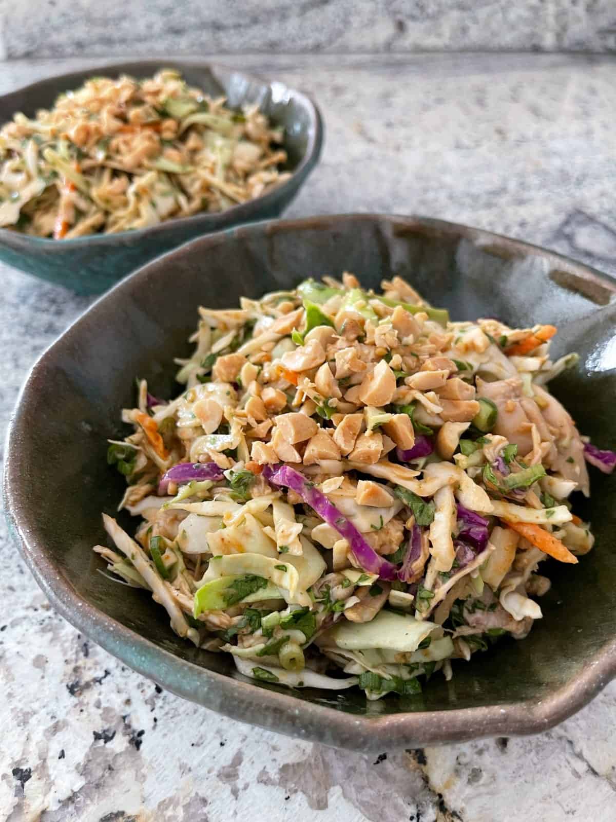 Thai cabbage salad with chicken in two green ceramic bowls on granite.