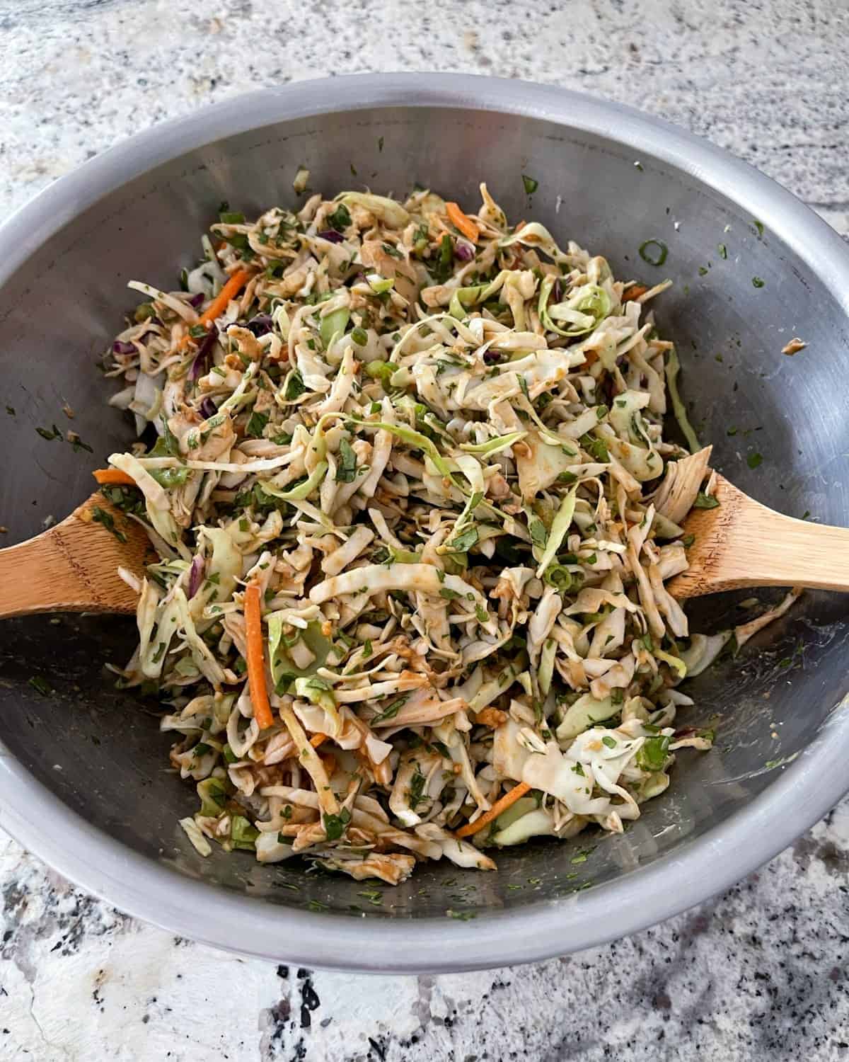 Tossing Thai chicken coleslaw in large bowl with two wooden spoons.