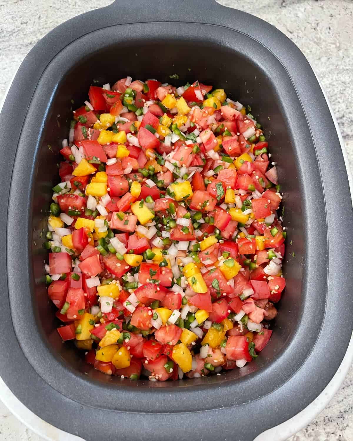Uncooked peach salsa - chopped tomatoes, peaches, jalapeno peppers, onion, minced garlic and cilantro - in black crock pot.