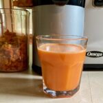Glass of fresh carrot beet pineapple juice on kitchen counter set in front of Omega Vertical Juices