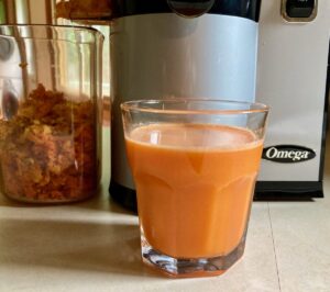 Glass of fresh carrot beet pineapple juice on kitchen counter set in front of Omega Vertical Juices