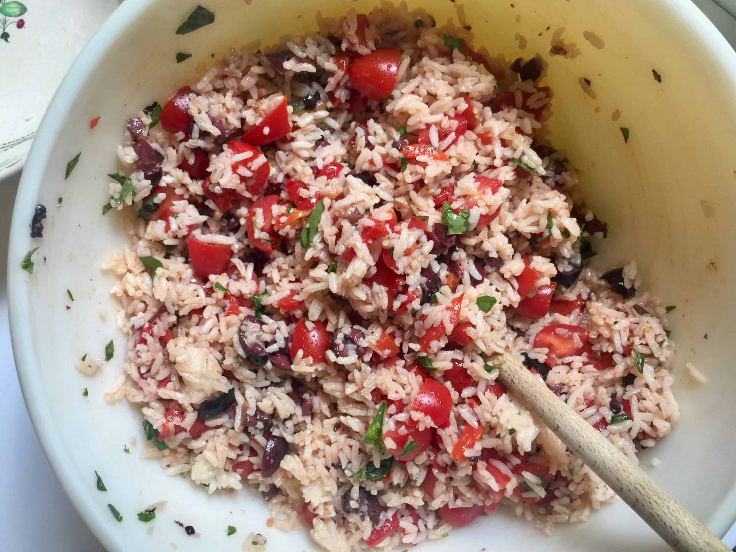 Mixing bowl with rice, chopped tomatoes, roasted bell peppers, olives, basil and anchovies.